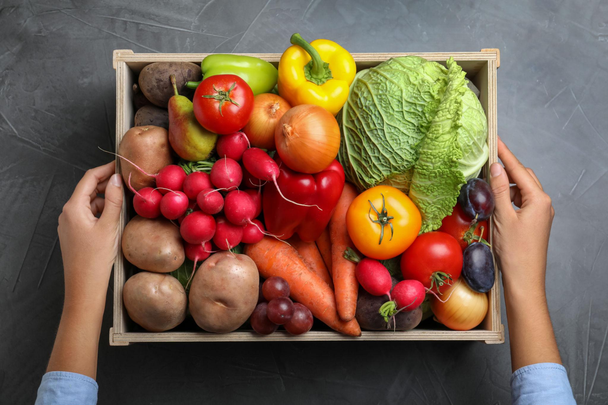 A crate of mixed produce held in two hands, viewed from above